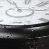 A close-up of a large, waterproof wall clock with water droplets on its surface and frame. The clock face shows Roman numerals, hands, and a thermometer/hygrometer dial. Produktbild-Vorschau