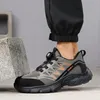 A person wearing black pants and a grey safety shoe, standing next to large rocks. Produktbild-Vorschau