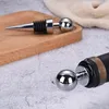 Close-up of two stainless steel bottle stoppers, one on a wooden cutting board and the other inserted into a wine bottle. Produktbild-Vorschau