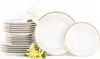 A stack of white dinner plates with gold trim and two decorative plates, accompanied by white and yellow flowers, on a white background. Náhľad obrázku produktu