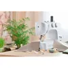 A white sewing machine is set up on a wooden table, with fabric and thread nearby, suggesting it's ready for use. Produktbild-Vorschau