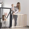 A woman is holding a baby while standing next to a wooden baby gate. Produktbild-Vorschau