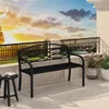 A black metal garden bench on a tiled patio with a railing and potted plants in the background, under a sunset sky. Produktbild-Vorschau