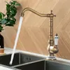 A vintage-style kitchen faucet with water running into a double sink, with a plant in the background. Náhľad obrázku produktu