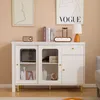 A white sideboard with gold legs and brass handles, decorated with books, a lamp, and decorative items. Anteprima dell’immagine prodotto