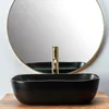 A black vessel sink with a gold faucet is shown in front of a round mirror. Náhľad obrázku produktu