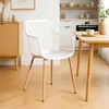 A modern white dining chair with wooden legs is placed next to a wooden cabinet in a bright, airy room with a kitchen in the background. Produktbild-Vorschau
