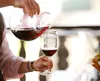 A person is pouring red wine from a decanter into a wine glass. Produktbild-Vorschau