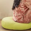 A person sitting on a round lime green floor cushion. Produktbild-Vorschau