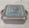 A square ceramic baking dish with a lid and handles, set against a light gray textured background. Náhled obrázku produktu