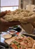A close-up shot of hands holding a flatbread, with small pizzas and dipping sauces in the background. Produktbild-Vorschau