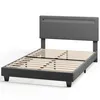 A grey upholstered bed frame with a wooden slat mattress support system, shown from a three-quarter angle against a white background. Anteprima dell’immagine prodotto