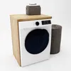A washing machine is placed on a wooden cabinet, with a laundry basket and a box of folded towels next to it. Voir les images du produit