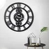 A large, black, metal wall clock with Roman numerals and visible gears is mounted on a white wall. Náhľad obrázku produktu