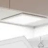 A square LED panel light is installed on a ceiling, with cabinets above it. Náhled obrázku produktu