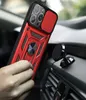 A hand holding a red and black iPhone 13 Pro case with a magnetic ring stand and camera cover, placed near a car's air vent with a magnetic car mount. Produktbild-Vorschau