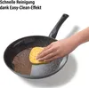 A hand is cleaning a frying pan with a sponge. Produktbild-Vorschau
