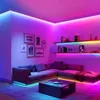 A living room with a sectional sofa, coffee table, and shelves, all illuminated by colorful LED strip lights. Produktbild-Vorschau