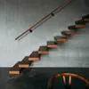 A modern staircase with wooden steps and a wooden handrail against a textured gray wall. Anteprima dell’immagine prodotto