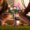 Rosa und gelbe LED-Blumen-Solar-Gartenleuchte mit grünen Blättern auf einem schwarzen Pfahl, im Gras mit Personen im Hintergrund Anteprima dell’immagine prodotto
