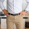 A man wearing a light blue dress shirt, tan pants, and a black belt with a metal buckle, with his hands on his hips. Anteprima dell’immagine prodotto