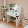 A white vanity table with a mirror and lights, decorated with various beauty products and accessories, set in a room with a plant and a bedside table. Produktbild-Vorschau