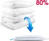 A stack of white pillows and a folded white duvet are shown, with a blue arrow indicating compression into a vacuum-sealed bag at the bottom. Náhled obrázku produktu