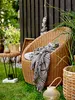 A cozy outdoor seating area with a wicker chair and blanket. Náhľad obrázku produktu