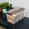 A clear plastic storage box filled with small brown paper bags containing various food items, placed on a black surface next to some plants and bottles. Anteprima dell’immagine prodotto