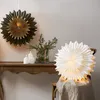 Two paper star lanterns are displayed, one hanging and one on a chair, with candles and greenery on a wooden table. Podgląd zdjęcia produktu