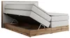 A king-size boxspring bed with its storage compartment open, revealing the interior and lifting mechanism. The bed has a white upholstered headboard and white mattress base, with a wood-effect frame in Wotan Oak. Produktbild-Vorschau