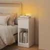 A white bedside table with books and a small decorative item is placed next to a bed.