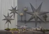 A collection of grey paper star lanterns are displayed in a festive, indoor setting, with gifts and greenery. Podgląd zdjęcia produktu