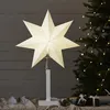A white star-shaped lamp on a stand, placed on a table with gifts and a Christmas tree in the background. Podgląd zdjęcia produktu