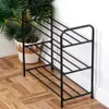 A black metal shoe rack with three shelves is shown in a room with wooden flooring and a potted plant. Produktbild-Vorschau