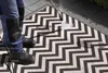 A person is pressure washing an outdoor rug with a zigzag pattern. Voir les images du produit