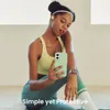 A woman in athletic wear is sitting on the floor, holding a green phone and looking at it. Anteprima dell’immagine prodotto