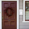 A close-up view of a brown front door with a wreath and a white mailbox mounted on the wall next to it. Náhled obrázku produktu