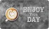 A cup of coffee with latte art and text that says "ENJOY YOUR DAY" on a chalkboard background. Produktbild-Vorschau
