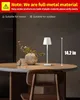A white table lamp is placed on a round table next to a vase of flowers. Produktbild-Vorschau