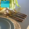 A set of copper-colored cutlery is arranged on a table setting with a woven placemat and a plate. Produktbild-Vorschau