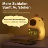A cute capybara-shaped alarm clock with a digital display is shown on a nightstand next to a smartphone. Produktbild-Vorschau