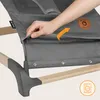A hand is shown adjusting the fabric of a baby bouncer. A washing machine icon is visible in the bottom right corner. Produktbild-Vorschau