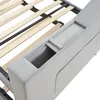 A close-up view of the side of a grey upholstered bed frame, showing a built-in storage compartment and the wooden slats of the bed base. Produktbild-Vorschau