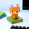 A Minecraft fox figurine sits on a grassy block base on a desk, next to a stack of books and a keyboard. Náhled obrázku produktu