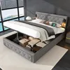 A bed with its storage compartment open, revealing various items stored inside. The bed is in a bedroom setting with a large window overlooking a body of water. Produktbild-Vorschau