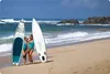 Two women in swimsuits stand on a sandy beach next to two stand-up paddleboards. Náhled obrázku produktu