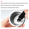 A hand is holding a coffee capsule and cleaning its bottom with a small brush. Produktbild-Vorschau
