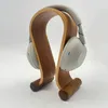A pair of silver headphones rests on a wooden headphone stand. Produktbild-Vorschau