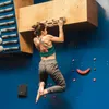 Eine Person trainiert an einem VerticalBoard One von YY Vertical; das an einer blauen Kletterwand montiert ist. Die Person trägt ein grünes Sportoberteil und graue Trainingshose. Produktbild-Vorschau